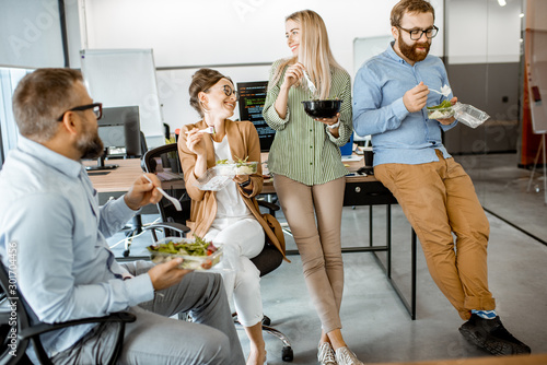 Photos Group of diverse colleagues eating takeaway salad, sitting together and having f
