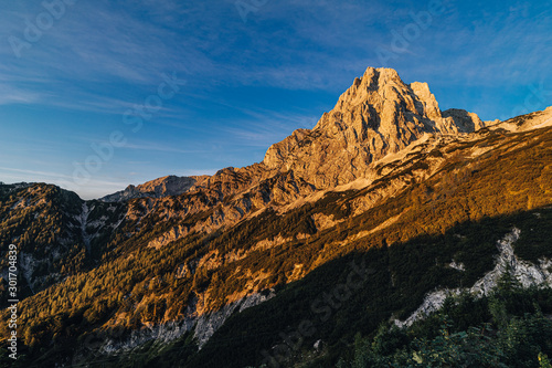 Fantastic view of a alpine mountain landscape of Totes Gebirge and the summit of Spitzmauer. Big rock wall  blue sky and mountains lid with orange sun. Sunrise or sunset mountain landscape  Austria.
