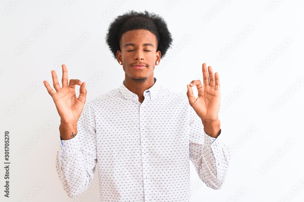 Young african american man wearing elegant shirt standing over isolated white background relax and smiling with eyes closed doing meditation gesture with fingers. Yoga concept. Young african american man wearing elegant shirt standing over isolated white background relax and smiling with eyes closed doing meditation gesture with fingers. Yoga concept.