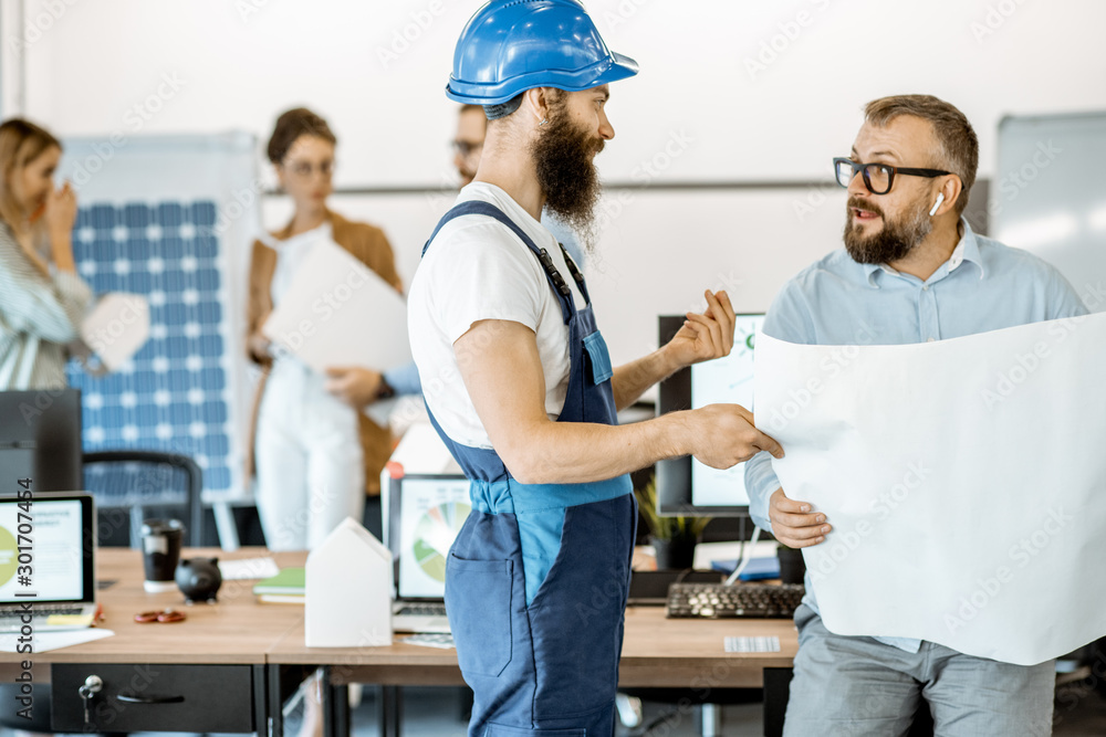 Obraz premium Senior foreman and workman in overalls working on project with blueprints in the office