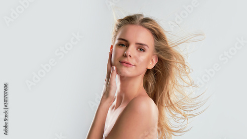 Beautiful young woman with clean perfect skin. Portrait of beauty model with natural nude make up and touching her face. Spa, skincare and wellness. Close up, blue background, copyspace