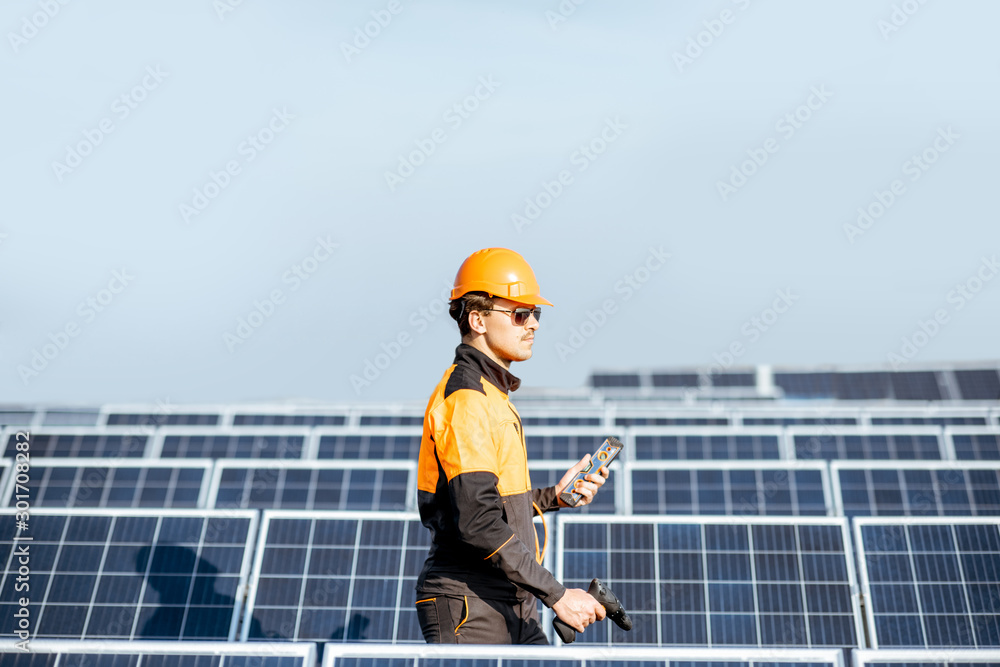 Well-equipped worker in protective orange clothing servicing solar panels on a photovoltaic rooftop plant. Concept of maintenance and installation of solar stations Well-equipped worker in protective orange clothing servicing solar panels on a photovoltaic rooftop plant. Concept of maintenance and installation of solar stations