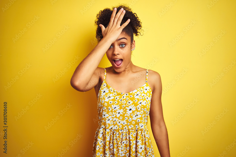 African american woman wearing casual floral dress standing over isolated yellow background surprised with hand on head for mistake, remember error. Forgot, bad memory concept. African american woman wearing casual floral dress standing over isolated yellow background surprised with hand on head for mistake, remember error. Forgot, bad memory concept.