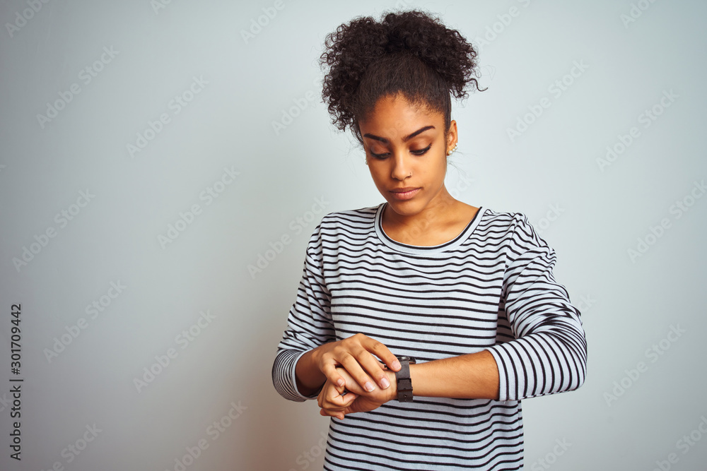 African american woman wearing navy striped t-shirt standing over isolated white background Checking the time on wrist watch, relaxed and confident African american woman wearing navy striped t-shirt standing over isolated white background Checking the time on wrist watch, relaxed and confident
