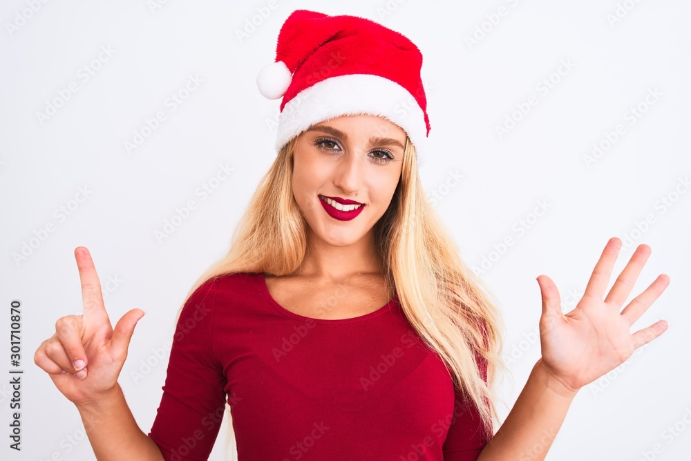 Young beautiful woman wearing Christmas Santa hat over isolated white background showing and pointing up with fingers number seven while smiling confident and happy. Young beautiful woman wearing Christmas Santa hat over isolated white background showing and pointing up with fingers number seven while smiling confident and happy.