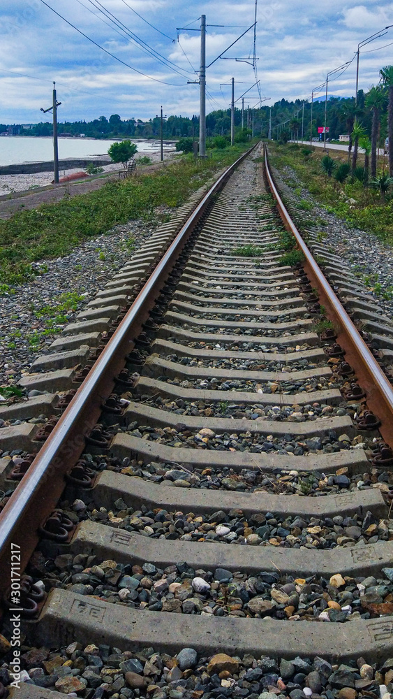 The railway tracks stretch into the distance under a blue sky with white fluffy clouds. The railway tracks stretch into the distance under a blue sky with white fluffy clouds.
