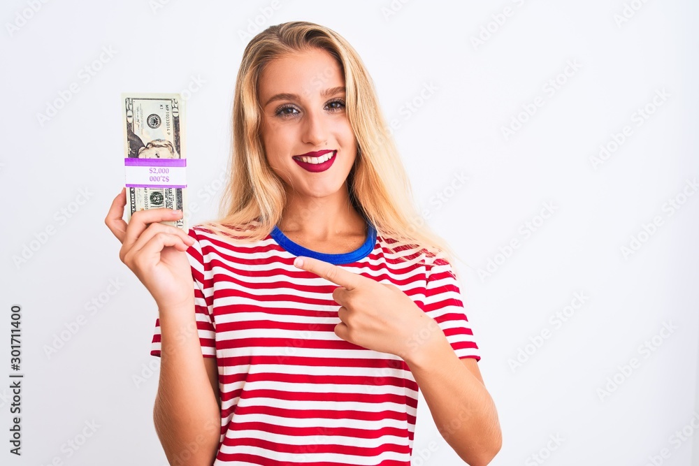 Beautiful woman wearing red striped t-shirt holding dollars over isolated white background very happy pointing with hand and finger Beautiful woman wearing red striped t-shirt holding dollars over isolated white background very happy pointing with hand and finger