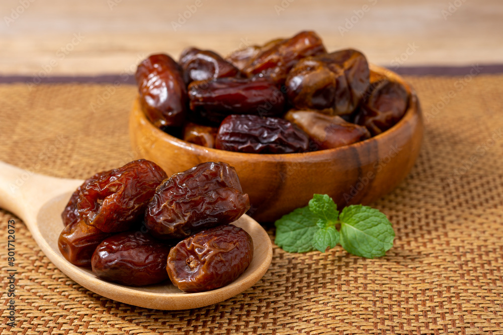 Closeup date palm fruits in wooden bowl and spoon with mint green leaf isolated on wood table background. Closeup date palm fruits in wooden bowl and spoon with mint green leaf isolated on wood table background.