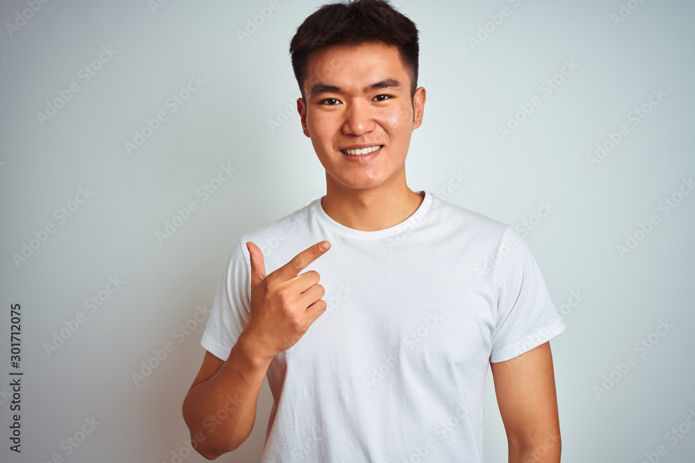 Young asian chinese man wearing t-shirt standing over isolated white background cheerful with a smile on face pointing with hand and finger up to the side with happy and natural expression Young asian chinese man wearing t-shirt standing over isolated white background cheerful with a smile on face pointing with hand and finger up to the side with happy and natural expression
