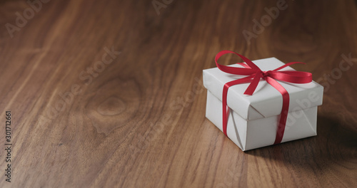 white gift box with red ribbon on walnut table