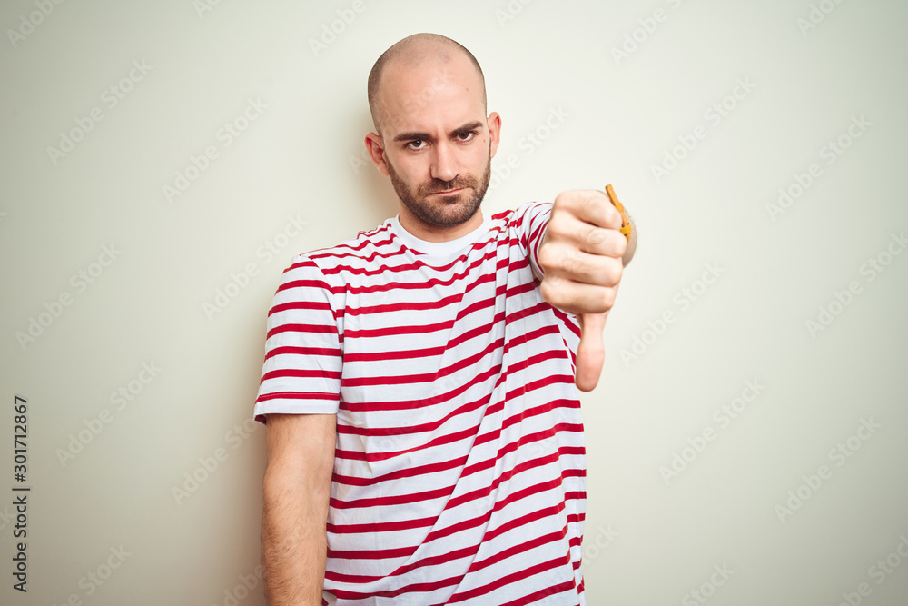 Naklejka premium Young bald man with beard wearing casual striped red t-shirt over white isolated background looking unhappy and angry showing rejection and negative with thumbs down gesture. Bad expression.