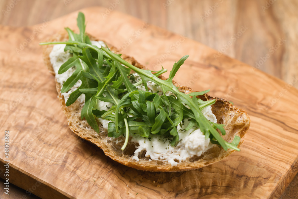 crunchy rustic bread with ricotta and arugula on olive wood board crunchy rustic bread with ricotta and arugula on olive wood board