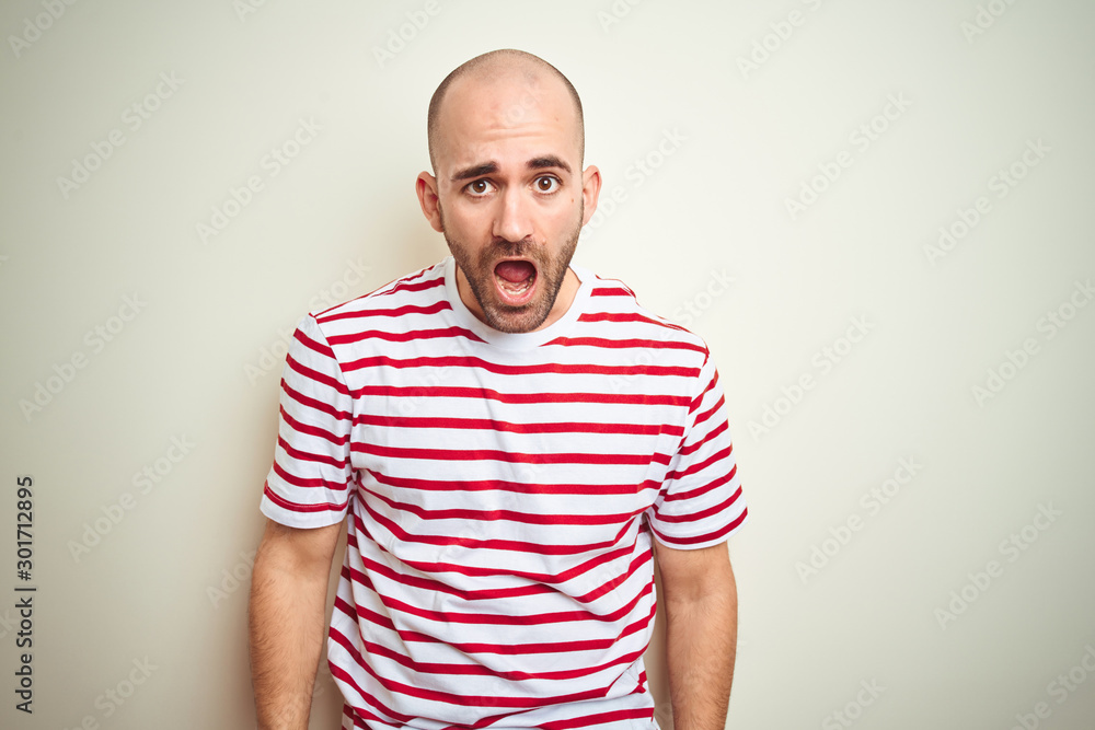 Young bald man with beard wearing casual striped red t-shirt over white isolated background In shock face, looking skeptical and sarcastic, surprised with open mouth Young bald man with beard wearing casual striped red t-shirt over white isolated background In shock face, looking skeptical and sarcastic, surprised with open mouth