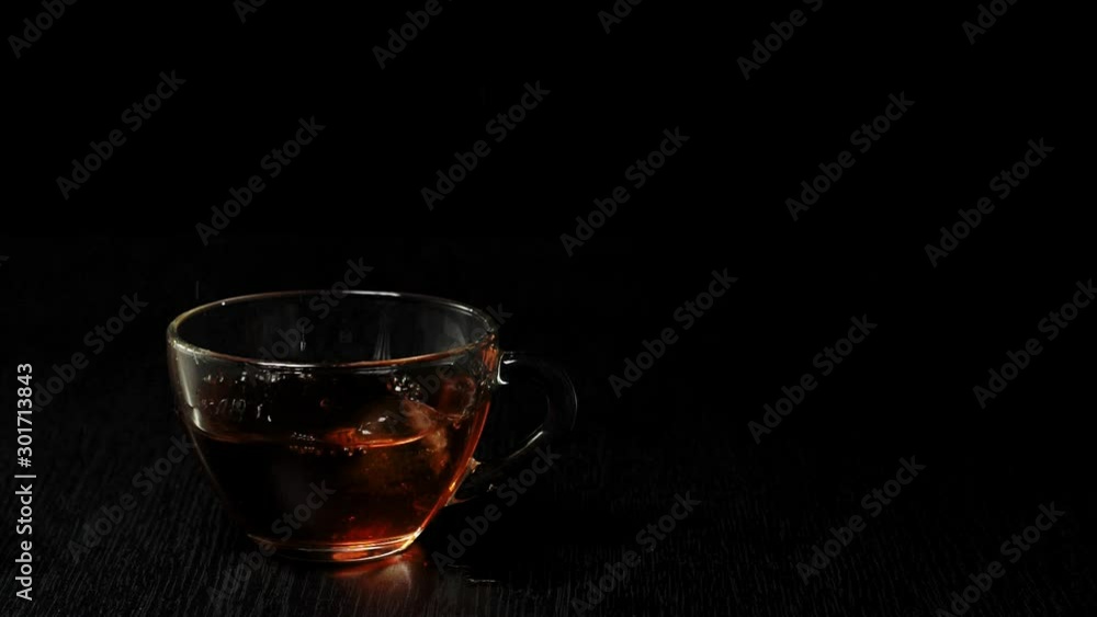 Tea ceremony. Ice cube falls into a transparent mug with fruit black tea on a black table against black background. Modern cold Chinese ceremony. Tea ceremony. Ice cube falls into a transparent mug with fruit black tea on a black table against black background. Modern cold Chinese ceremony.