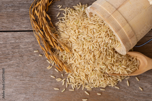 Brown rice or loonzain in wooden bucket and dry ear of rice or paddy isolated on old wood table background. Healthy food concept. Top view.Flat lay.