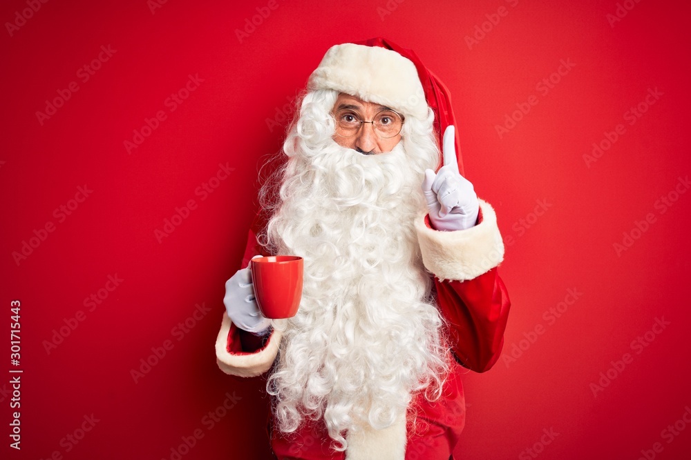 Senior man wearing Santa Claus costume holding cup of coffee over isolated red background surprised with an idea or question pointing finger with happy face, number one