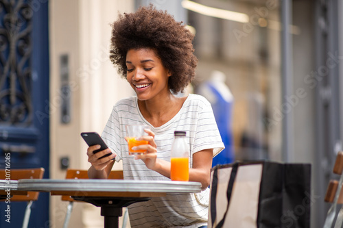 beautiful young black woman sitting at outdoor cafe with cellphone and drink