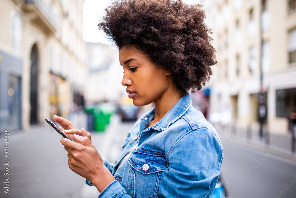 Side of young black woman with afro hair sending text message on cellphone - obrazy, fototapety, plakaty 