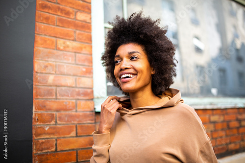 Candid close up of beautiful young black woman with afro hairstyle smiling outside against wall