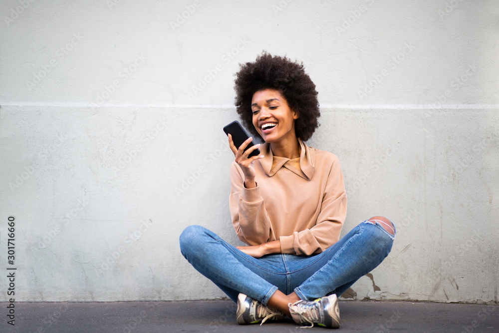 happy young african american woman sitting on floor with cellphone