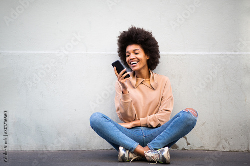 happy young african american woman sitting on floor with cellphone