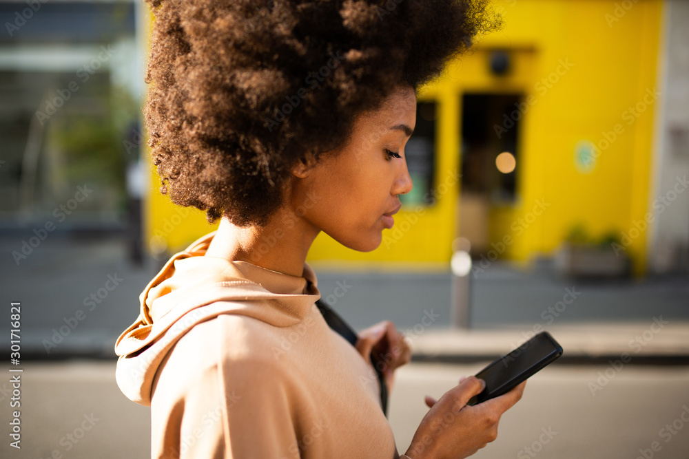 Close up side of beautiful young black woman with afro hairstyle walking with cellphone in city Close up side of beautiful young black woman with afro hairstyle walking with cellphone in city