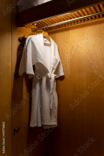 Closet white bathrobes and clothes hangers hanging on rack in the hotel wooden closet warm white low light.
