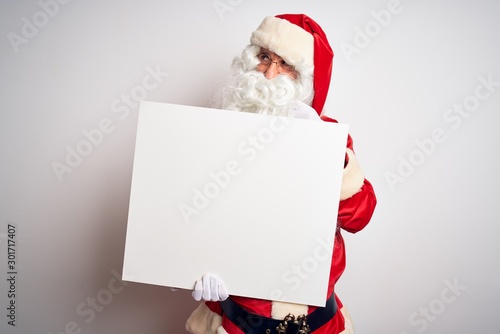Middle age man wearing Santa Claus costume holding banner over isolated white background serious face thinking about question, very confused idea