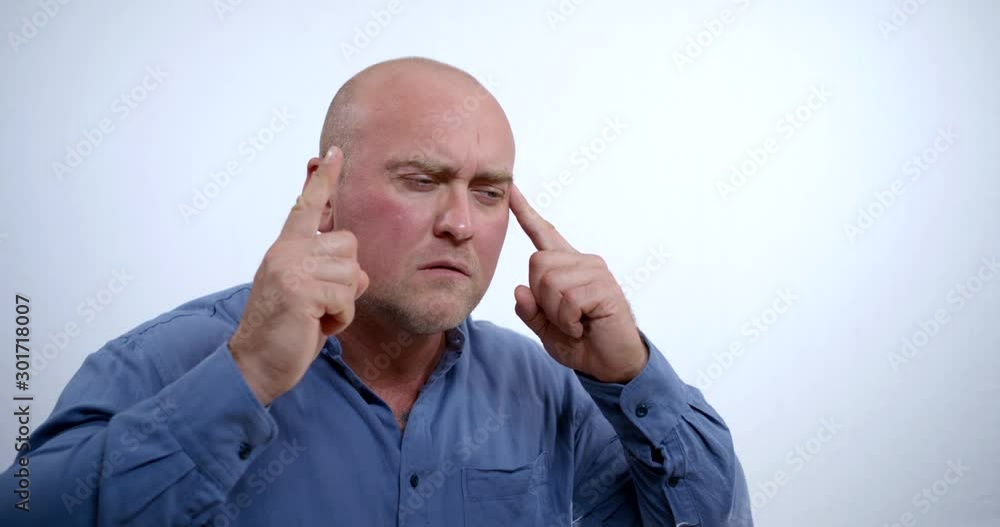 portrait of a large bald middle-aged man in a blue shirt on a white background. he tries to calm down, focus and make a decision. he rubs his temples with his fingers, raises his finger portrait of a large bald middle-aged man in a blue shirt on a white background. he tries to calm down, focus and make a decision. he rubs his temples with his fingers, raises his finger