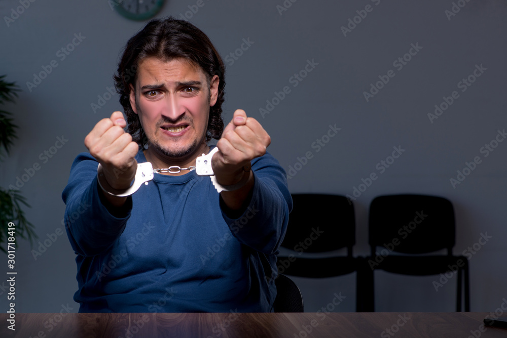 Young convict man sitting in dark room Young convict man sitting in dark room