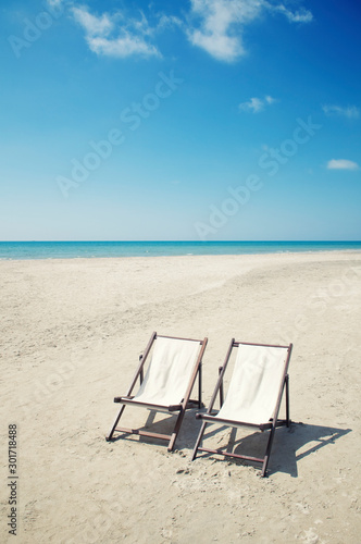 Fototapeta Naklejka Na Ścianę i Meble -  Pair of empty deck chairs sitting together on a deserted beach with calm blue sea on the  horizon