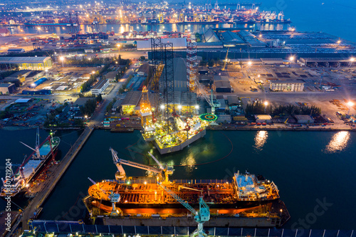 Aerial view of a jack up oil drilling rig and dry dock ship in the shipyard for maintenance during suset time.