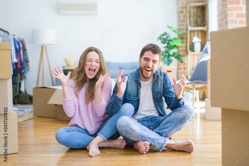 Young beautiful couple moving to a new house sitting on the floor celebrating mad and crazy for success with arms raised and closed eyes screaming excited. Winner concept Young beautiful couple moving to a new house sitting on the floor celebrating mad and crazy for success with arms raised and closed eyes screaming excited. Winner concept