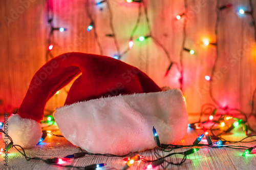 red santa claus hat  golden christmas balls and bells on a light background. rear multi-colored flashlights. bokeh background