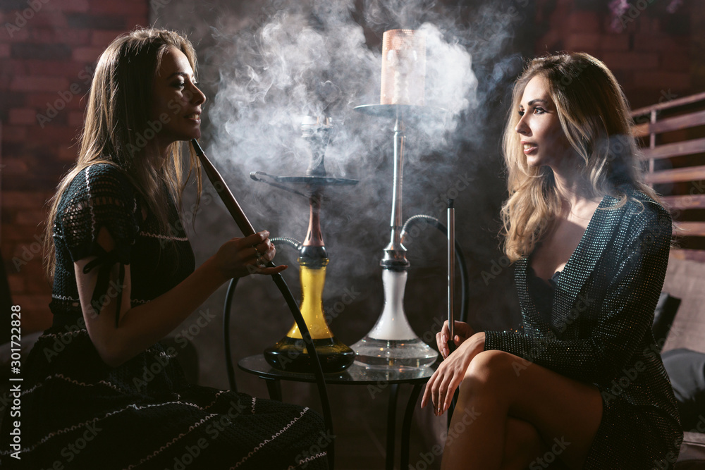 Girls party in hookah lounge. Group of two young women in backlight