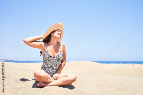Young beautiful woman sunbathing sitting on the sand wearing summer swinsuit at maspalomas dunes bech