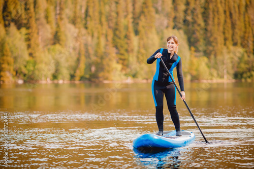 фотографія Girl in thermo clothing rowing oar on sup board blue lake water paddleboard back
