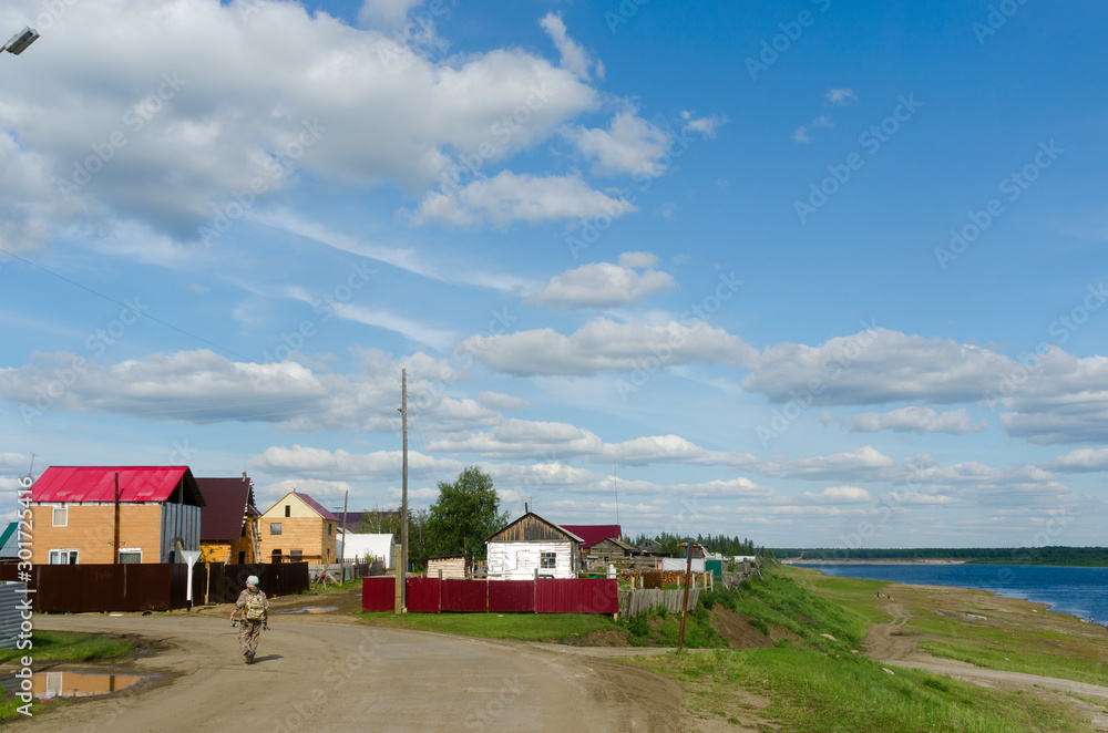 Yakut girl with a backpack and fishing rods is on the village road among the houses near the Northern river vilyu in Yakutia.