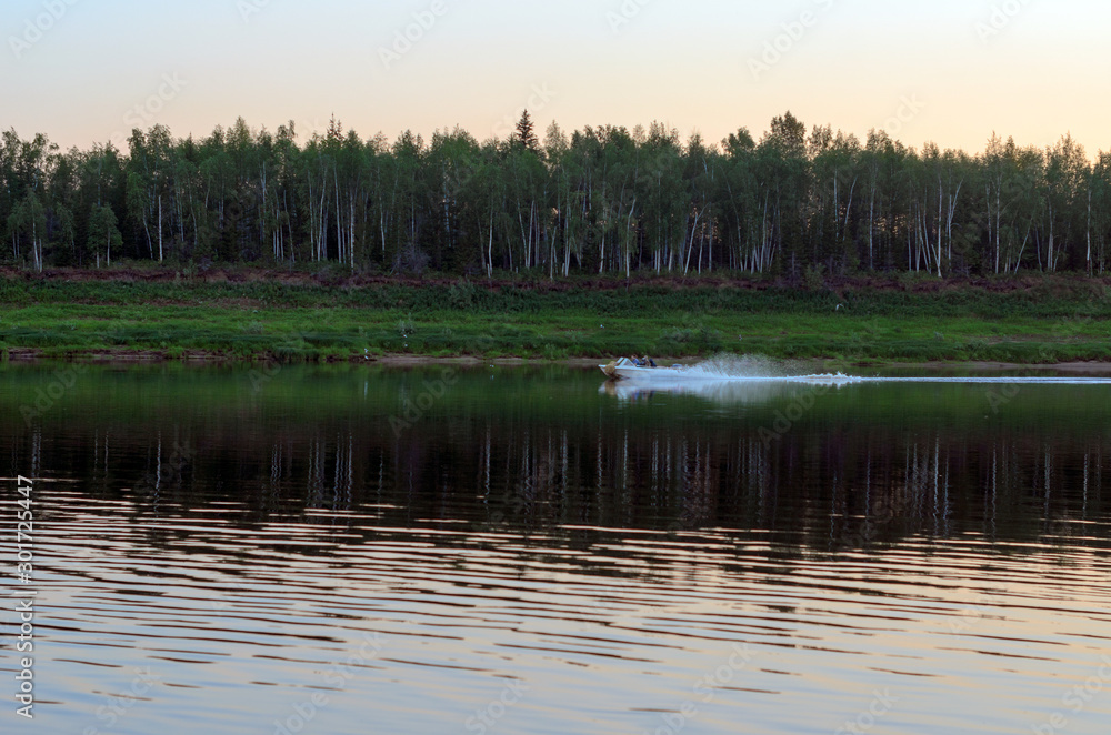 Boat with people going on the river Vilyuisk in the North of Yakutia on the background of the taiga spruce forest at sunset in the evening.