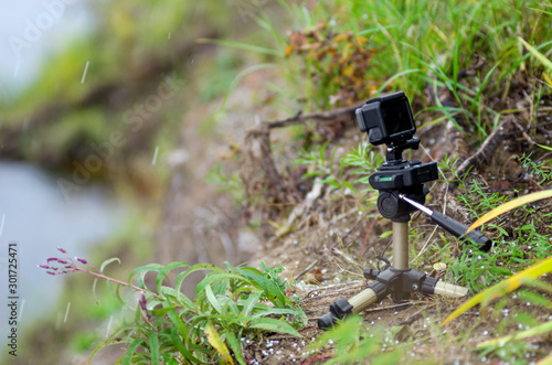 Action camera on a small tripod stands in the grass of the river under the flying snow flakes. photo