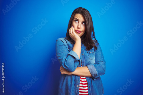 Young beautiful brunette woman wearing casual blue denim jacket over blue isolated background thinking looking tired and bored with depression problems with crossed arms.