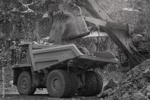 Excavator bucket close-up loads ore in the dump-body truck in a quarry  black and white. Mining industry. Mine and quarry equipment.