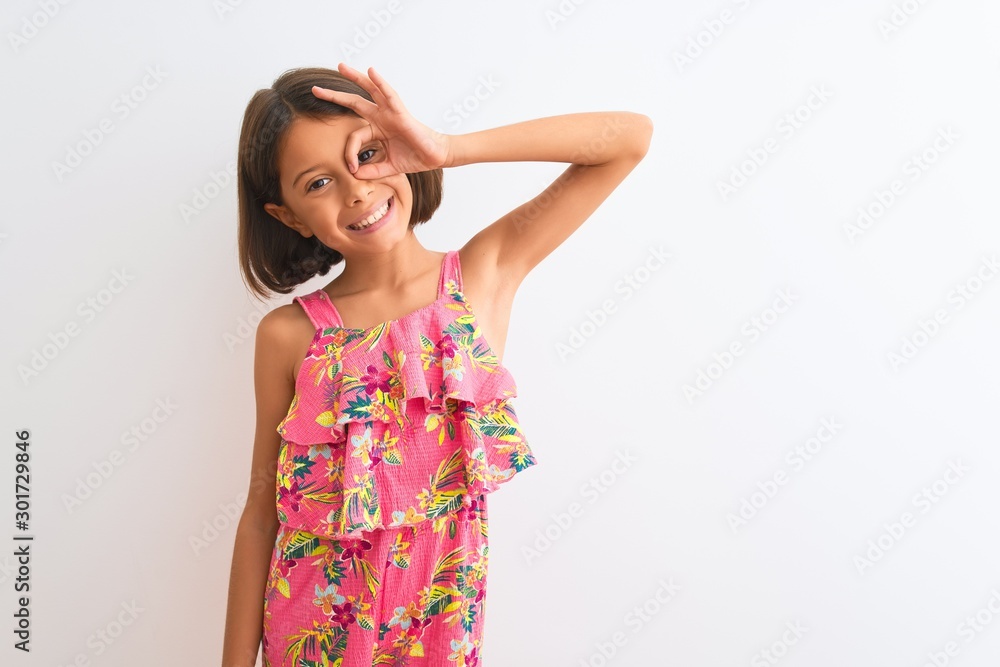 Young beautiful child girl wearing pink floral dress standing over isolated white background doing ok gesture with hand smiling, eye looking through fingers with happy face. Young beautiful child girl wearing pink floral dress standing over isolated white background doing ok gesture with hand smiling, eye looking through fingers with happy face.
