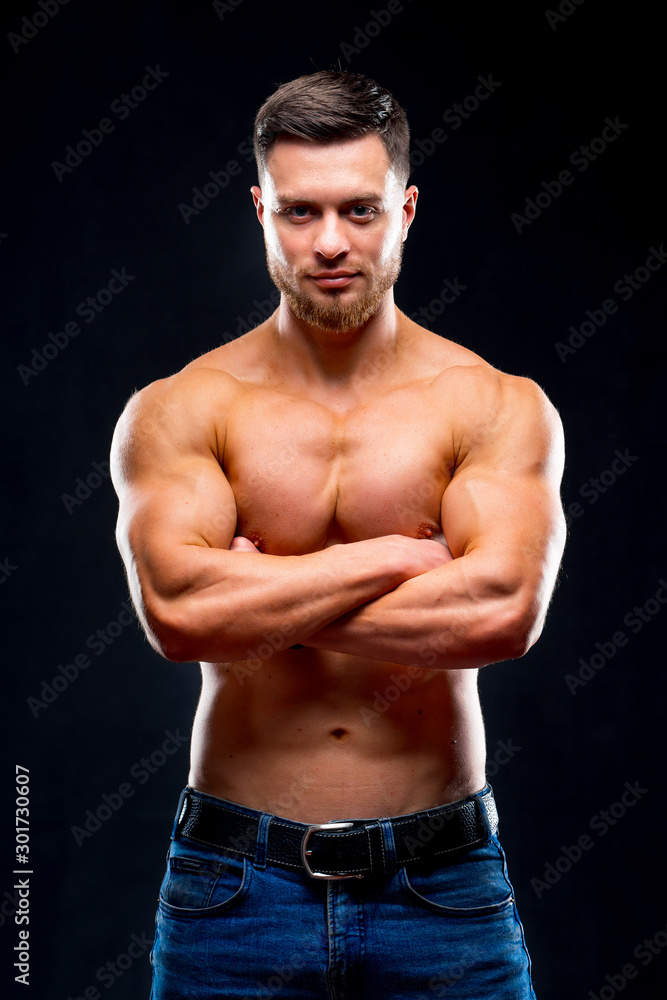 Obraz premium Portrait of a handsome guy with crossed hands over chest. Black background. Strong body and cool face. Studio Photoshoot. Closeup.
