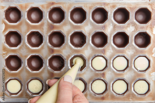 Production of chocolates. Chocolatier is pouring melted white chocolate mass into molds. Chocolate factory.