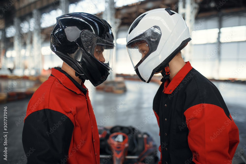 Two kart racers in helmets standing face to face - obrazy, fototapety, plakaty 