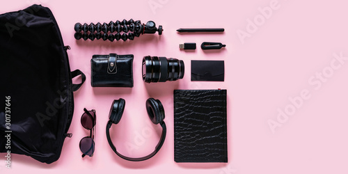 Stylish black accessories and modern gadgets on pink background, top view with copyspace. Trendy headphones, camera lens, wallet, sunglasses, notebook and bag on table, flat lay composition
