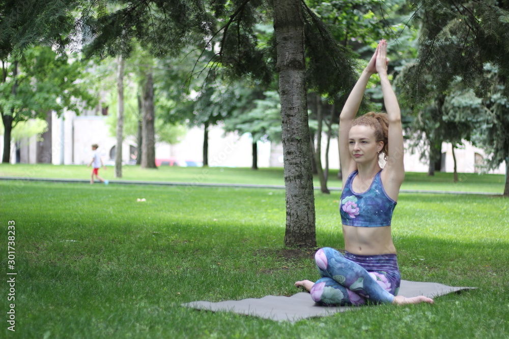 Obraz premium Girl with curly blond hair doing yoga outdoors in the park.
