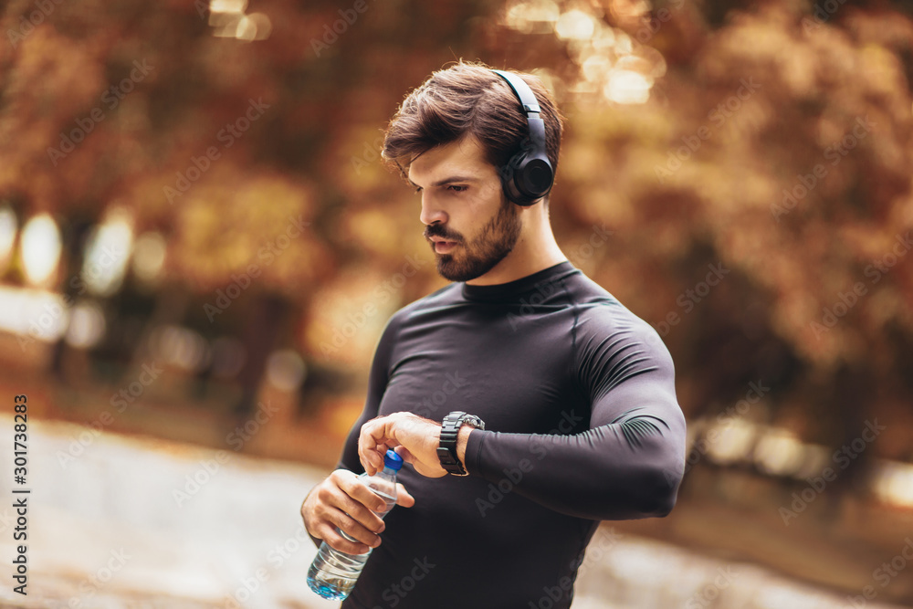 Portrait of  young man on a morning jogging in the autumn park, man listening to music with headphones - obrazy, fototapety, plakaty 