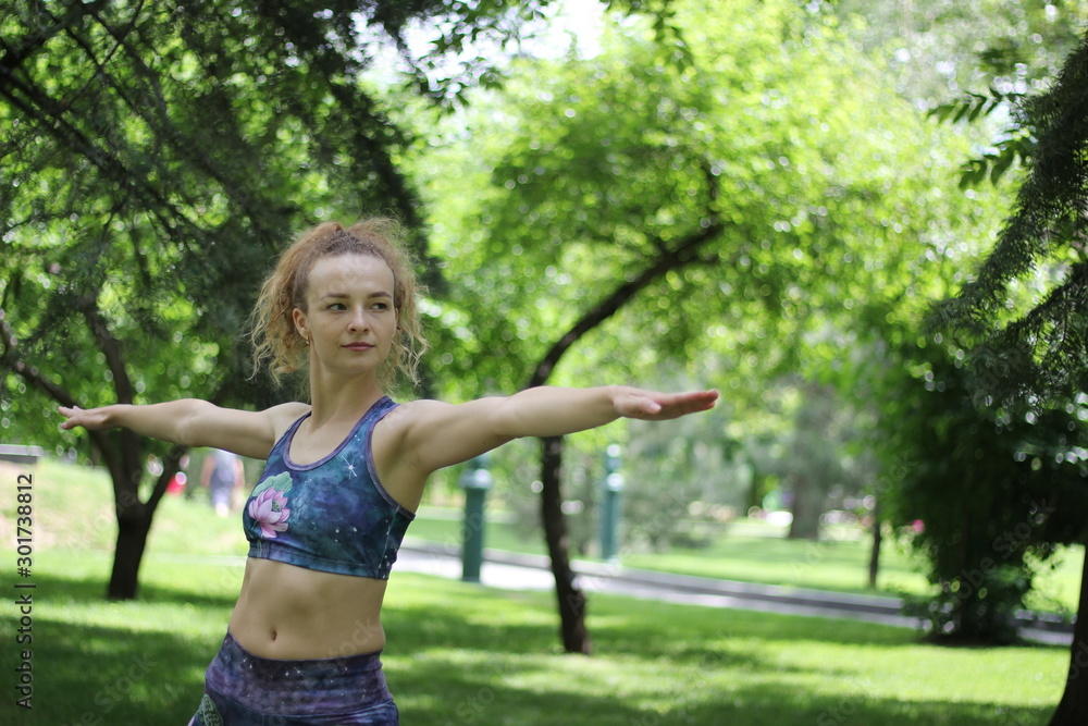 Girl with curly blond hair doing yoga outdoors in the park.